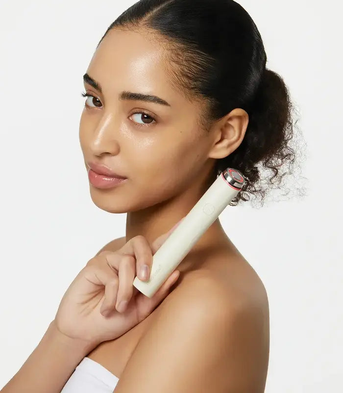 Woman holding a white electronic device against her shoulder on a light background